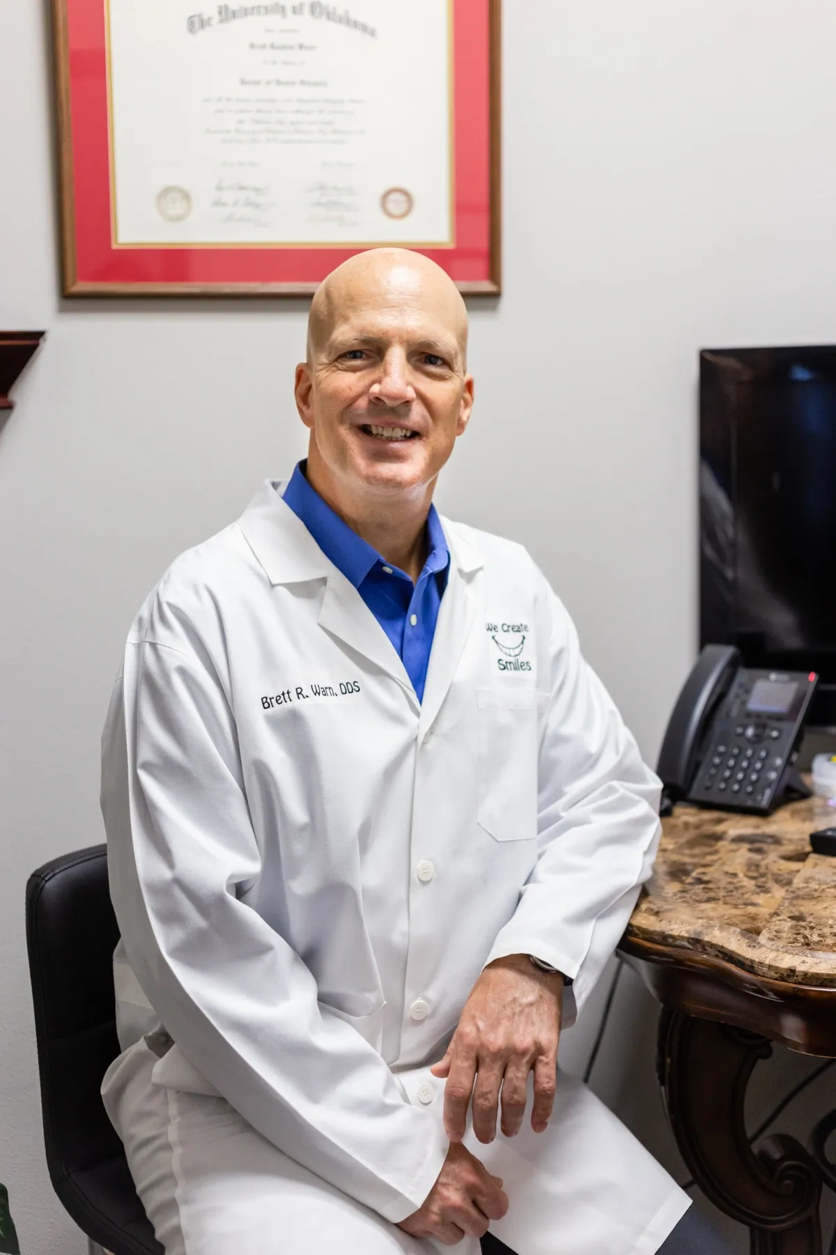 A man in white lab coat sitting at desk.